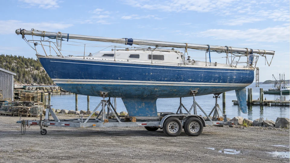 Illustration of blue and white sailboat secured on a trailer with its mast lowered along the deck