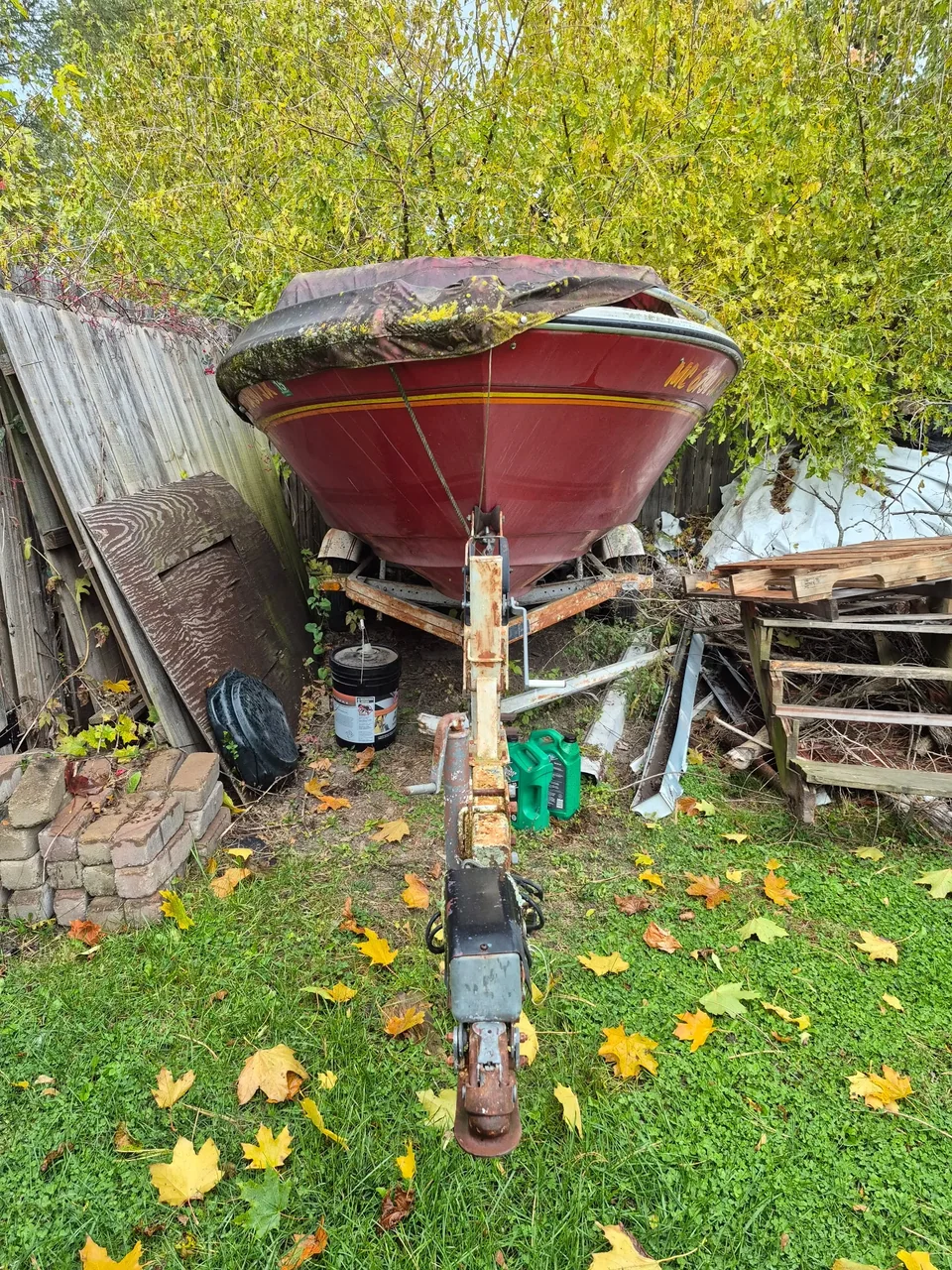 Bow of a red motorboat and its trailer beside a garden fence