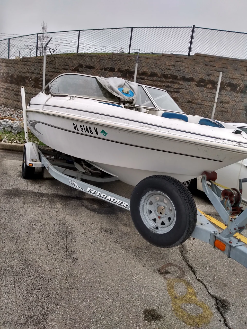 Compact white runabout on a trailer in a fenced gravel yard