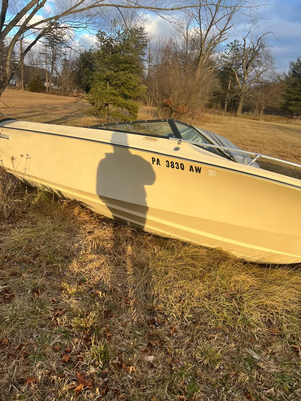 Side view of a yellow open boat beside leaf-covered ground