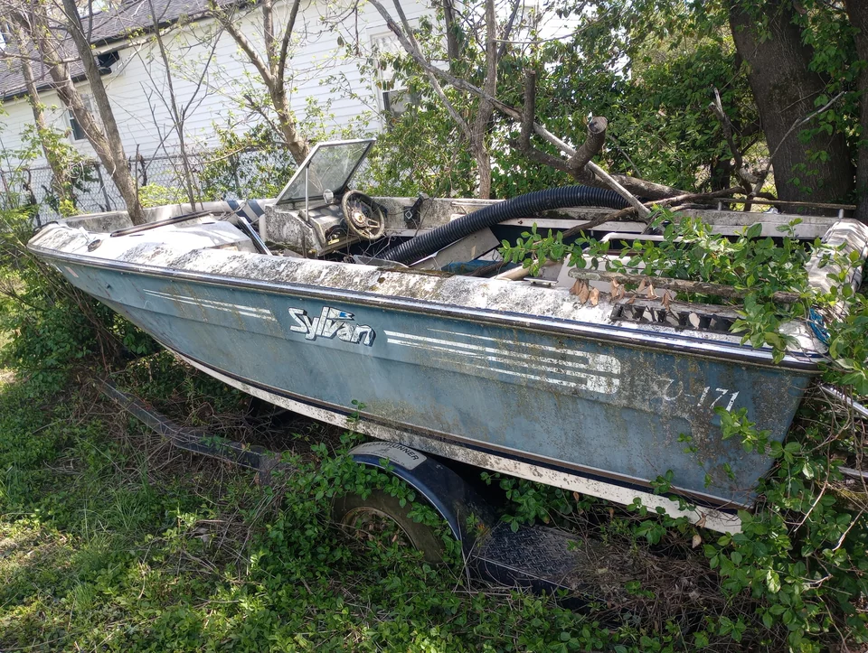 Weathered blue hull with loose materials inside, resting among trees