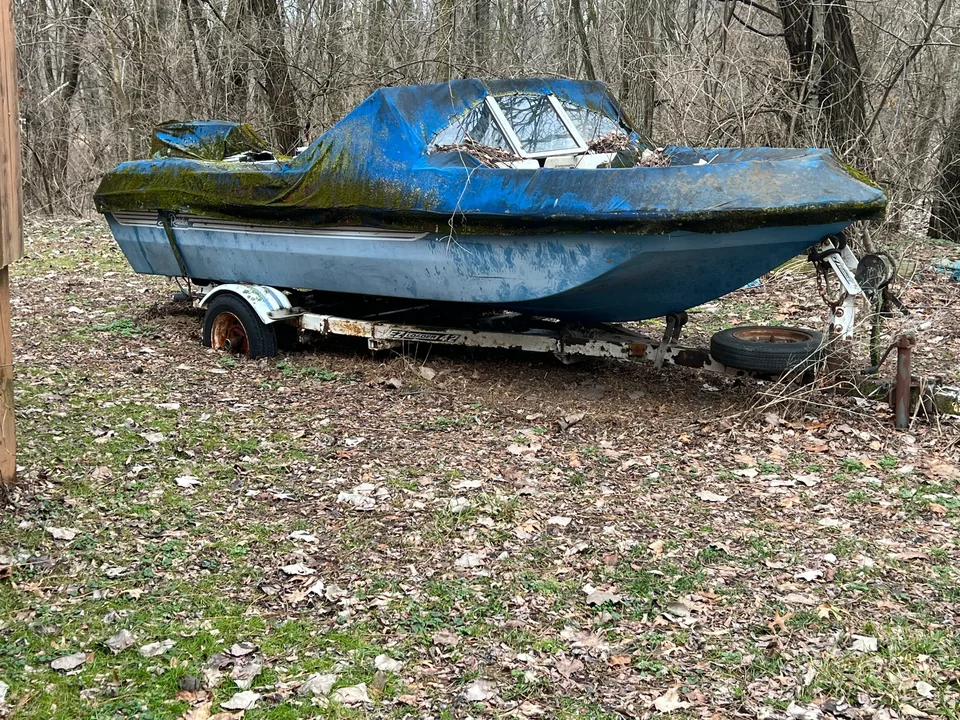 Weathered blue runabout on a trailer among fallen leaves
