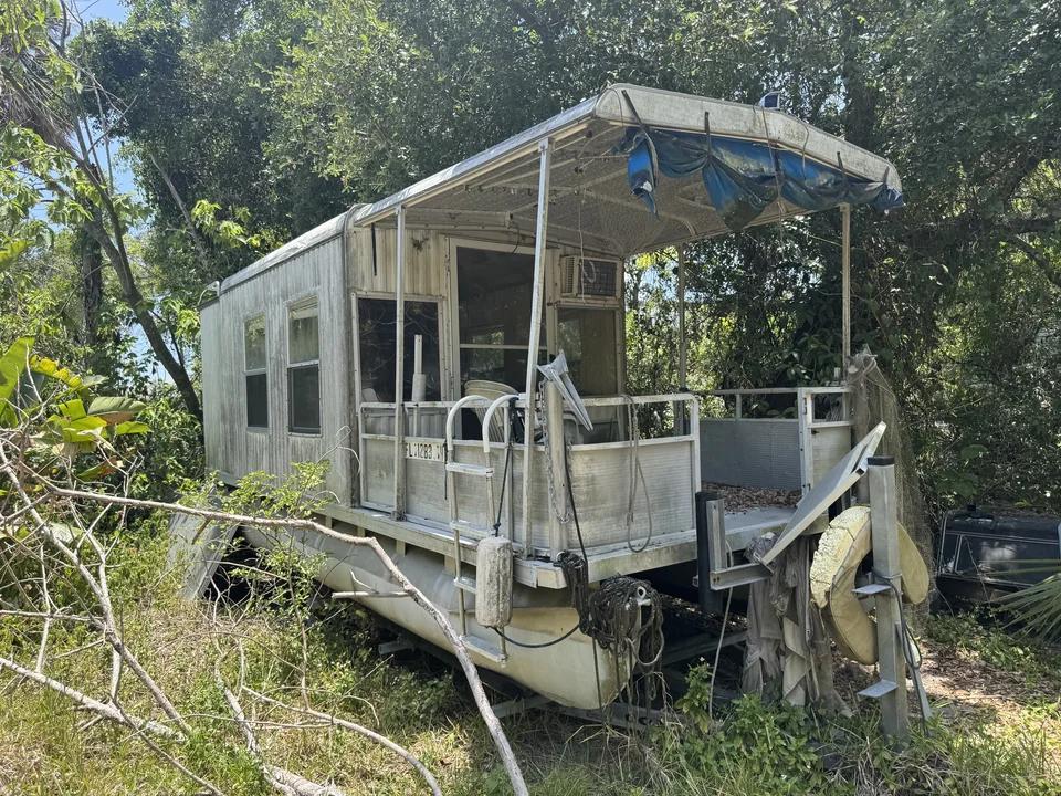 Weathered houseboat with a damaged roof beside dense vegetation