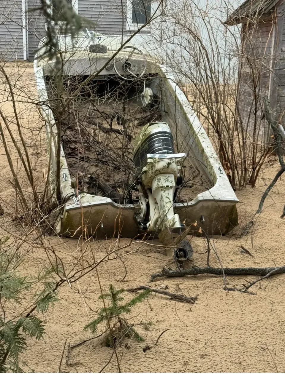 Weathered outboard boat standing beside a building and bare trees