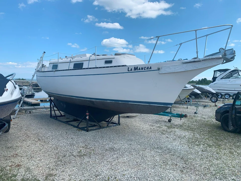 White sailboat supported on stands in a gravel boatyard