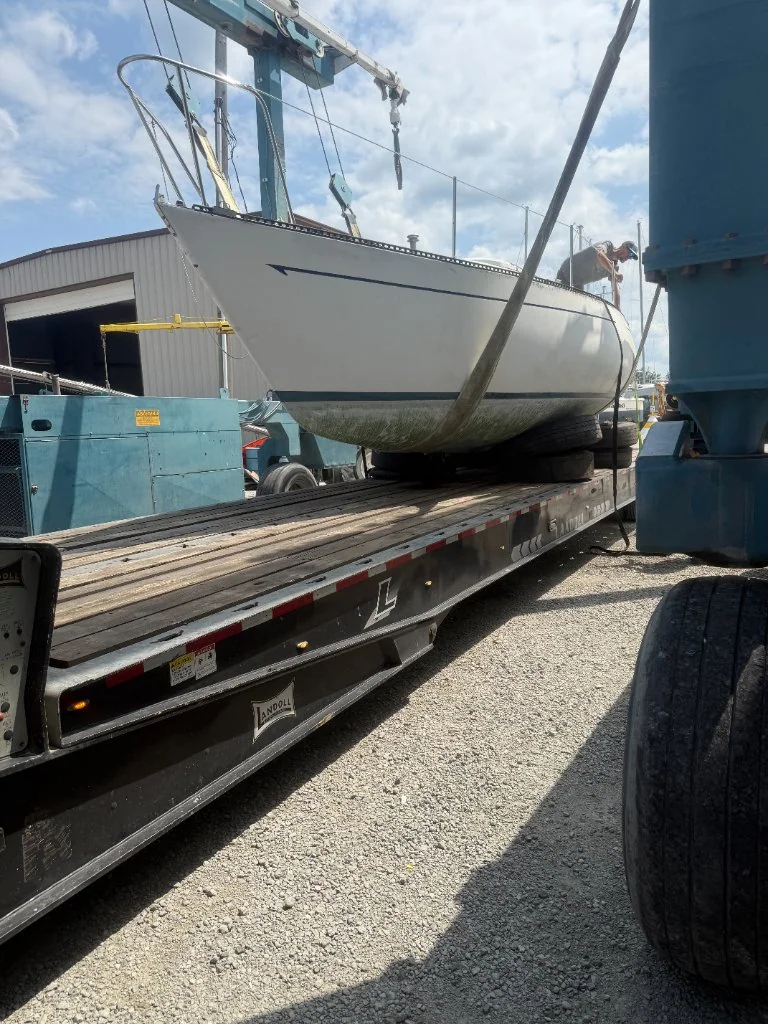 White sailing hull secured above a flatbed trailer