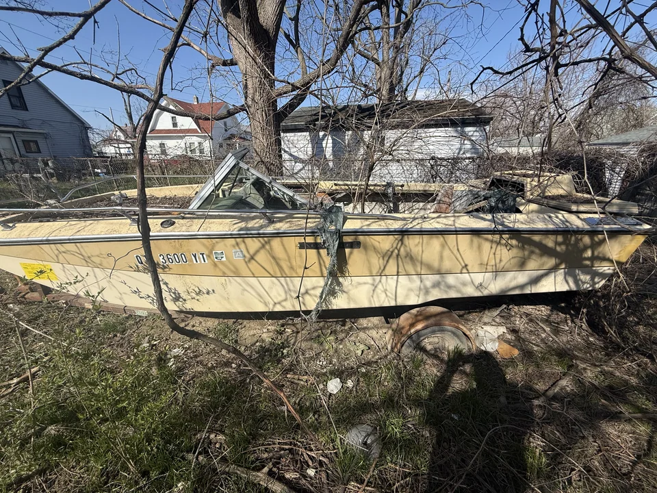 Yellowed boat hull surrounded by bare branches in a yard